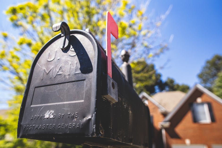 Close-up of a traditional US mailbox with a red flag in a sunny neighborhood.